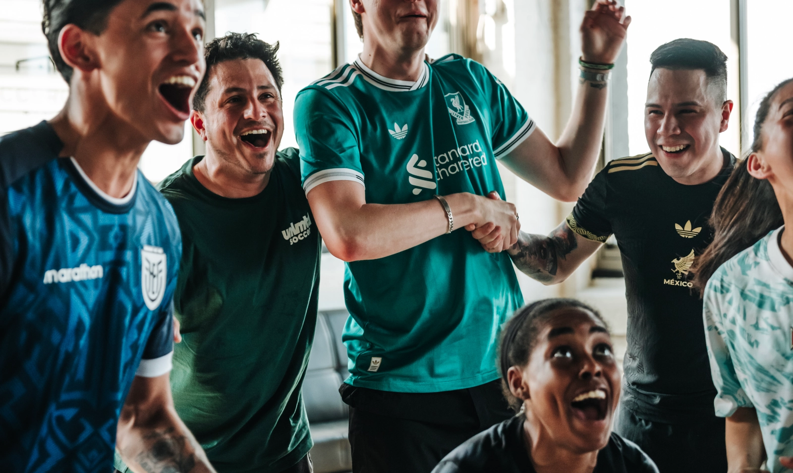 Un groupe d'amis divers célébrant ensemble tout en regardant un match de soccer dans un espace intérieur lumineux et moderne