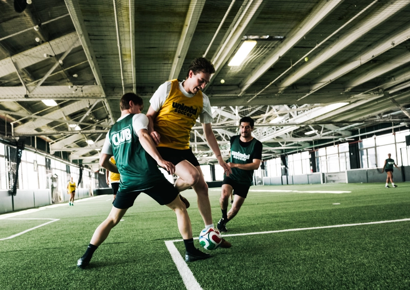 Des joueurs en maillots verts et jaunes s'affrontant pour le ballon lors d'un match de soccer en intérieur sur une pelouse