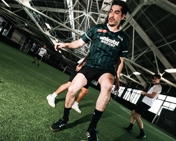 Un joueur de soccer en maillot vert contrôle un ballon coloré sur une pelouse artificielle à l'intérieur d'un grand espace