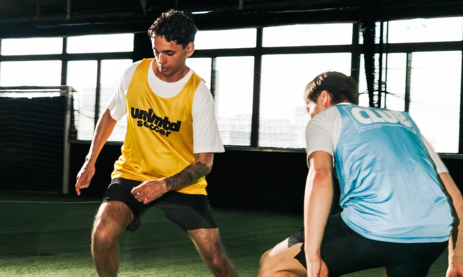 Deux joueurs de soccer en maillots d'entraînement pratiquent un exercice sur un terrain de gazon intérieur avec de grandes