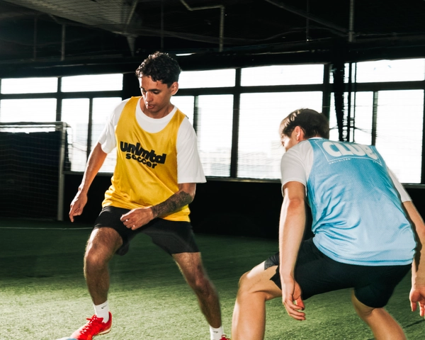 Deux joueurs de soccer en maillots d'entraînement pratiquent un exercice sur un terrain de gazon intérieur avec de grandes
