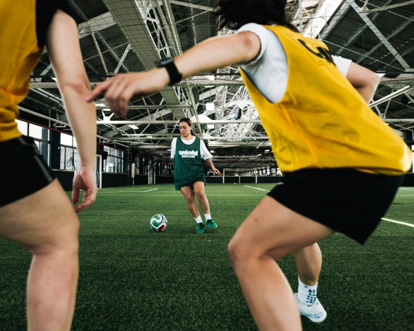 Jeunes joueurs de soccer en gilets jaunes et maillot vert s'entraînent sur un terrain de gazon artificiel en intérieur avec