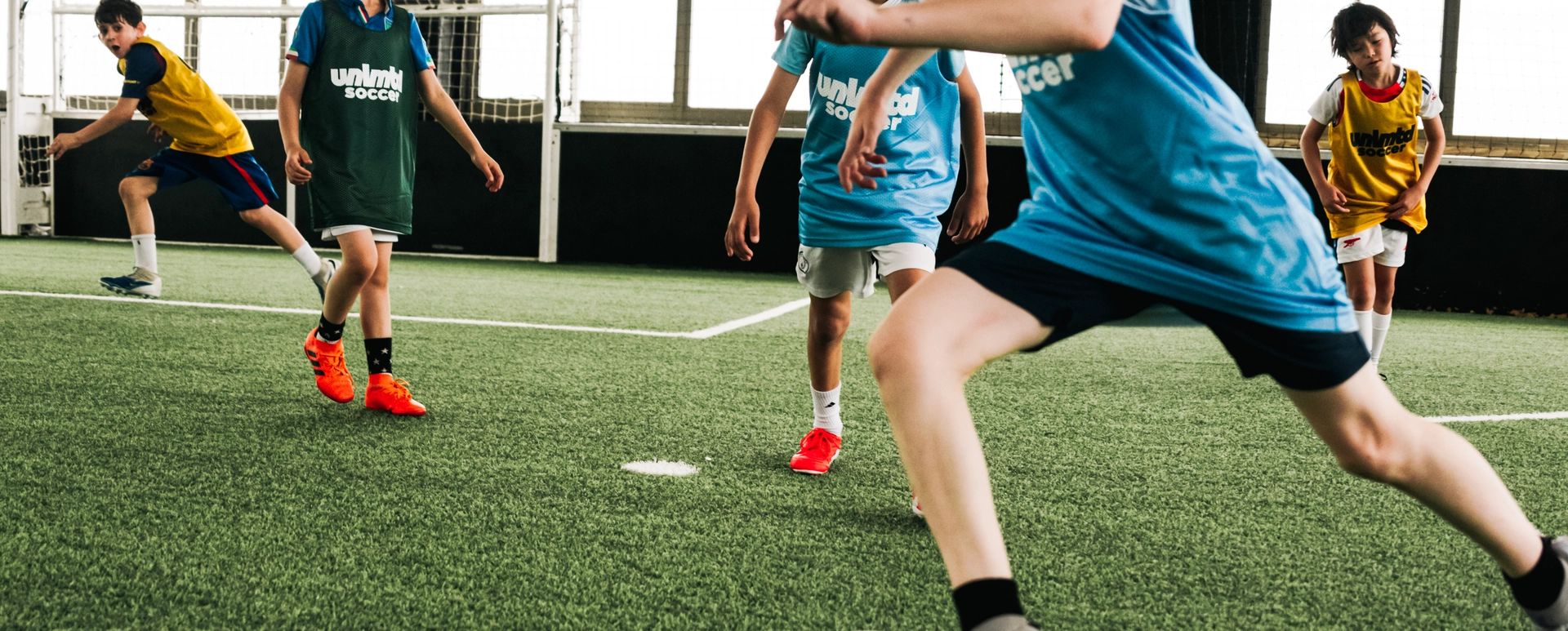 Young players in blue and yellow jerseys actively engaged in an indoor soccer training session on artificial turf, with one