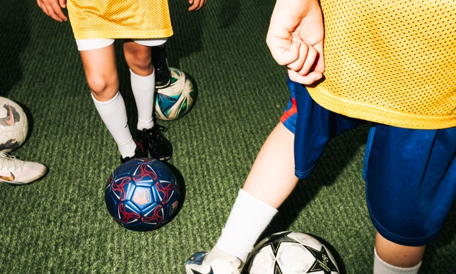 Young soccer players in yellow training bibs practice with soccer balls on artificial turf at an unlimited soccer facility.