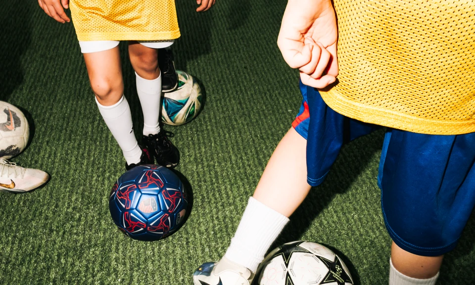 Young soccer players in yellow training bibs practice with soccer balls on artificial turf at an unlimited soccer facility.