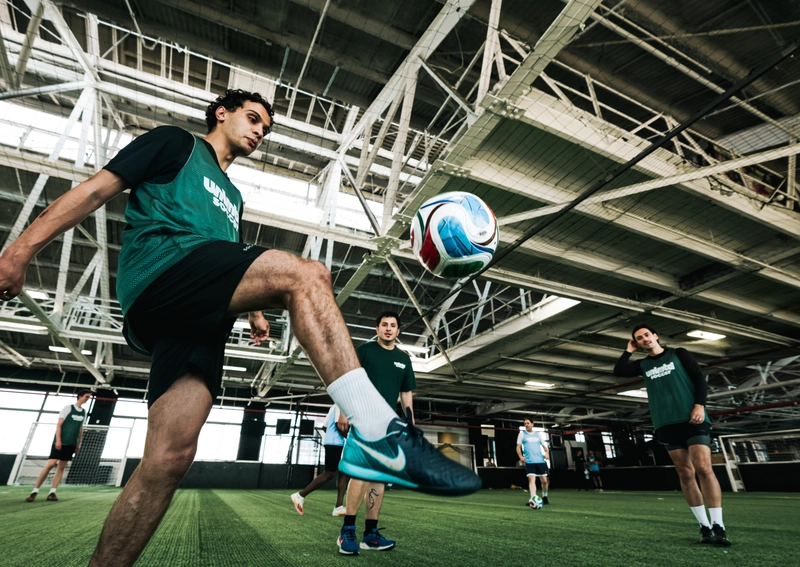Des joueurs de soccer s'entraînant en intérieur sur une pelouse artificielle dans un grand complexe sportif de style