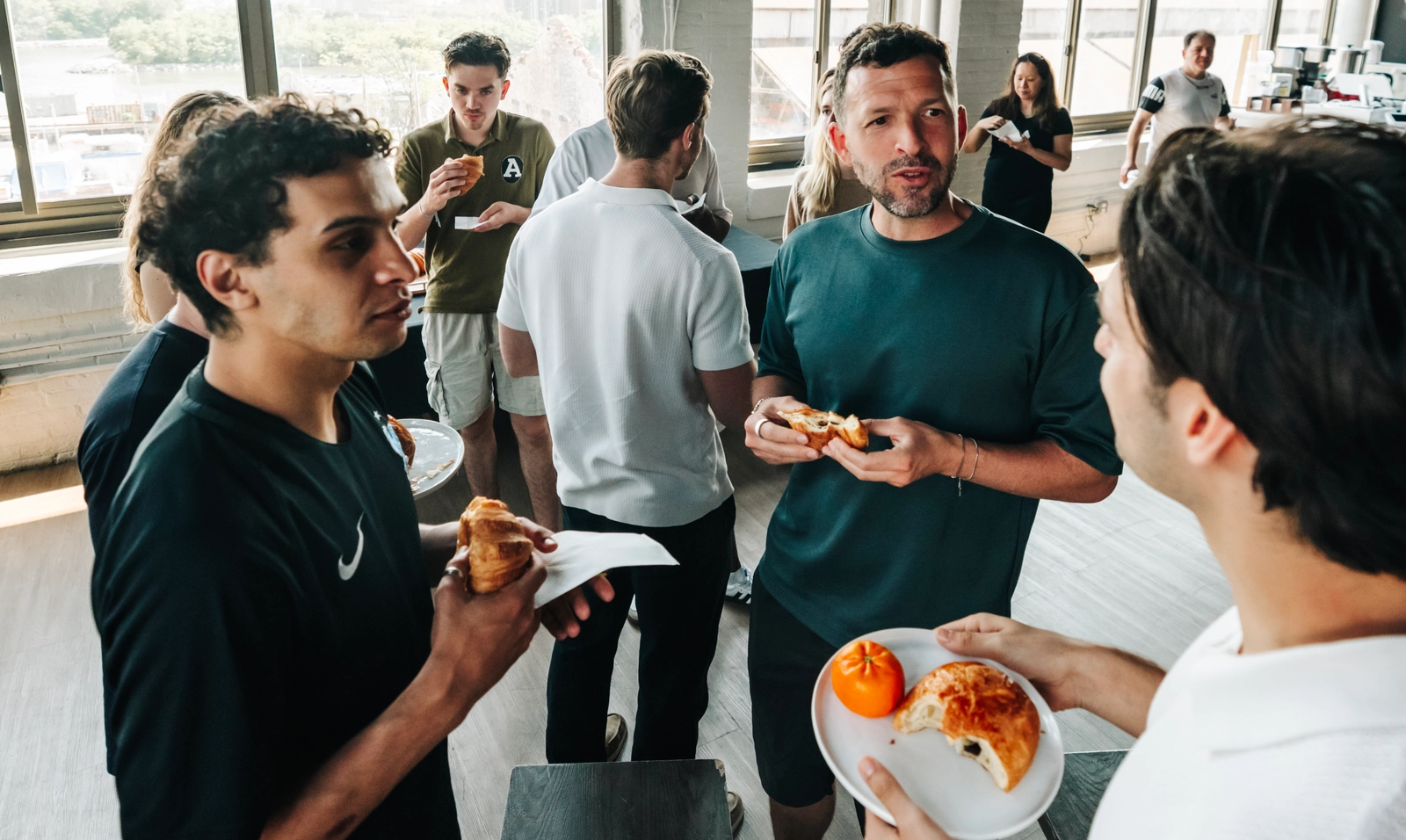 Un groupe de membres d'une équipe de soccer socialisant et mangeant des pâtisseries dans un salon de bureau lumineux et