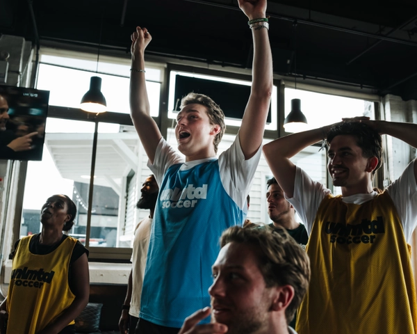 Un groupe de personnes en maillots Unlimited Soccer célébrant à l'intérieur d'un lieu moderne avec de grandes fenêtres et