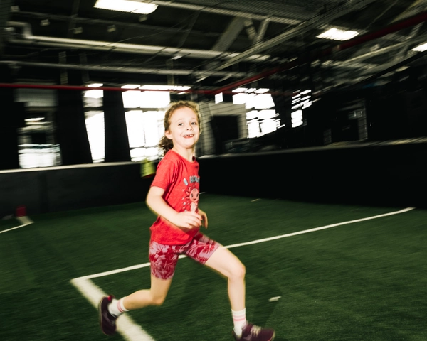 Une jeune fille en T-shirt rouge et short à motif court avec énergie sur un terrain de soccer intérieur avec gazon