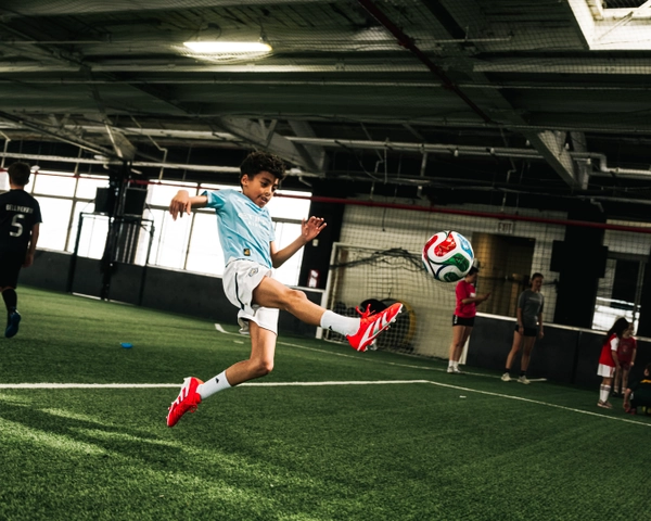 Un jeune joueur de soccer en maillot bleu clair et chaussures rouges saute pour frapper un ballon de soccer coloré sur un