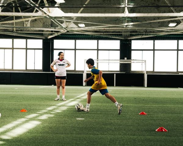 Un jeune joueur de soccer en maillot jaune dribble un ballon autour de cônes pendant un entraînement sur un terrain de gazon